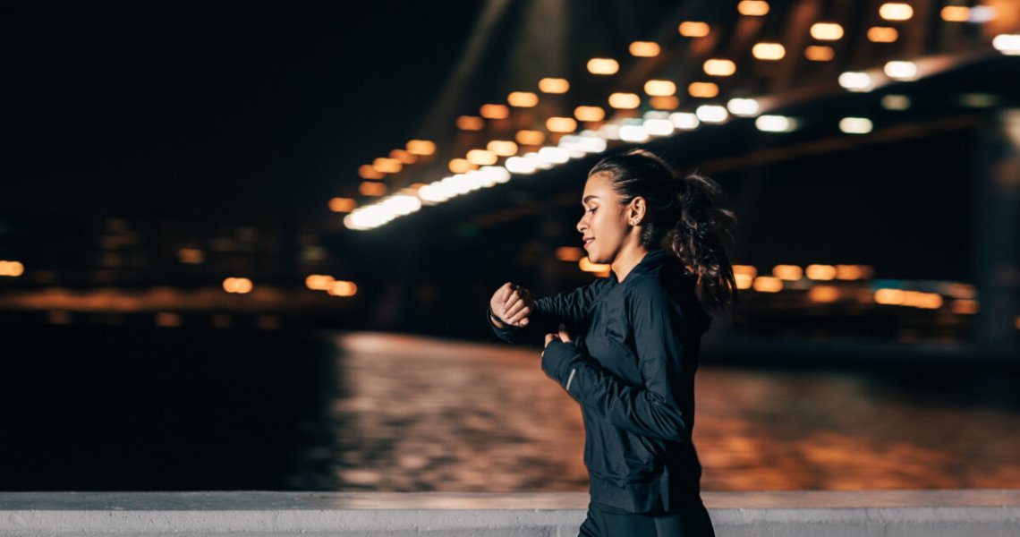 Young middle east woman jogging at night looking in fitness tracker on her wrist